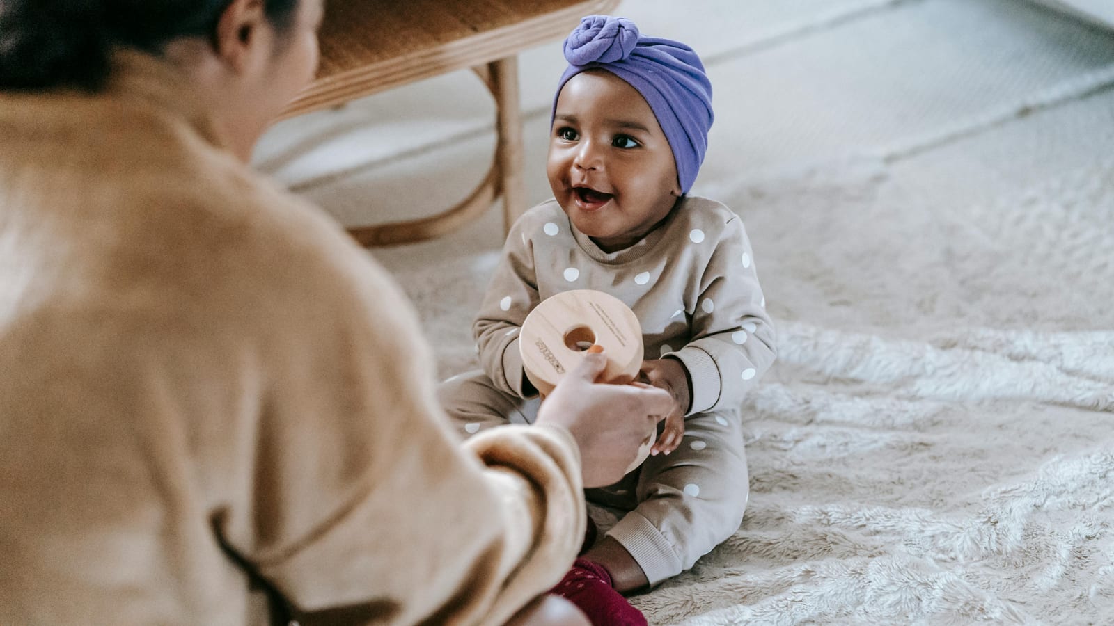 A Black mother kneeling beside her toddler as the child takes early steps in a sunlit room